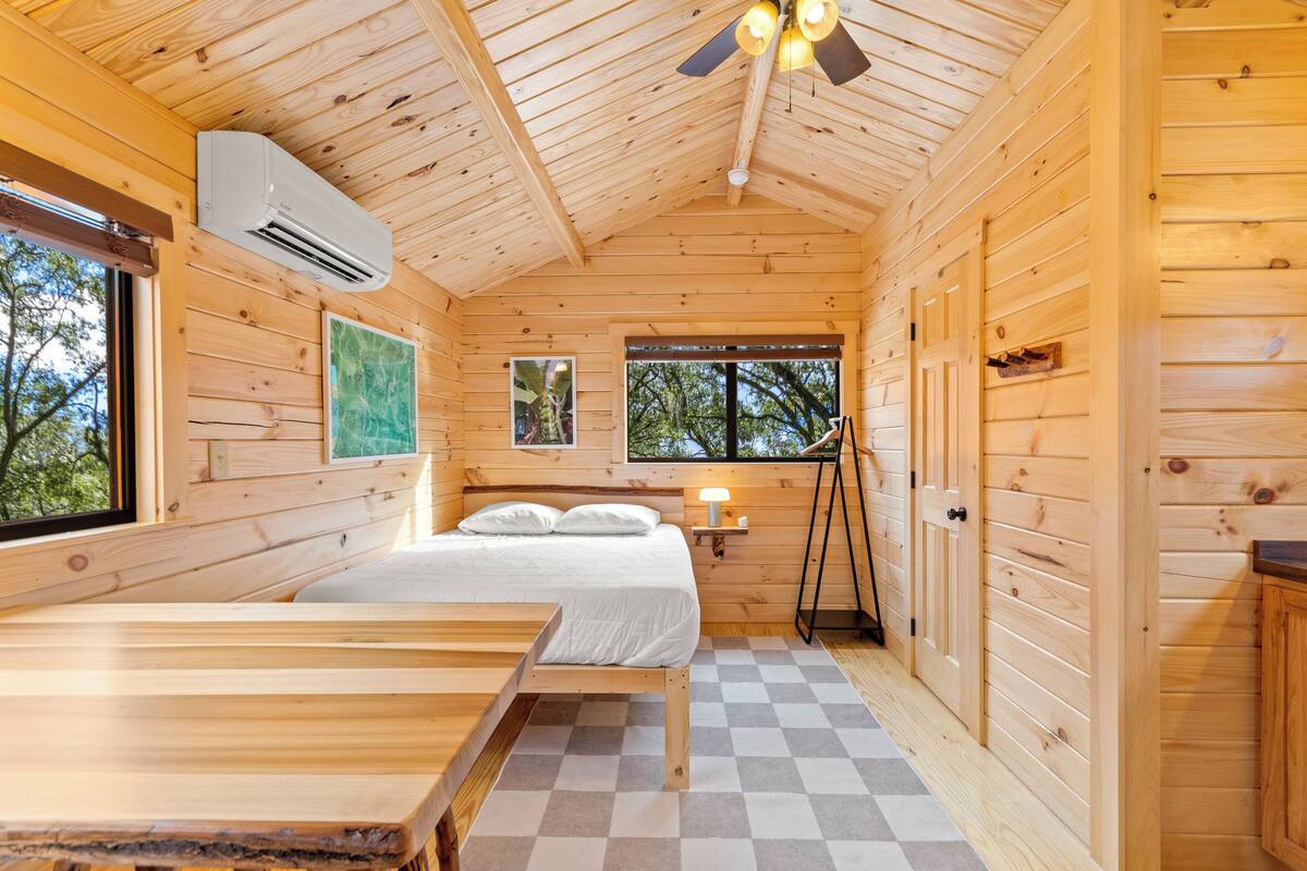 A wooden cabin with a bed, a desk, and a window.