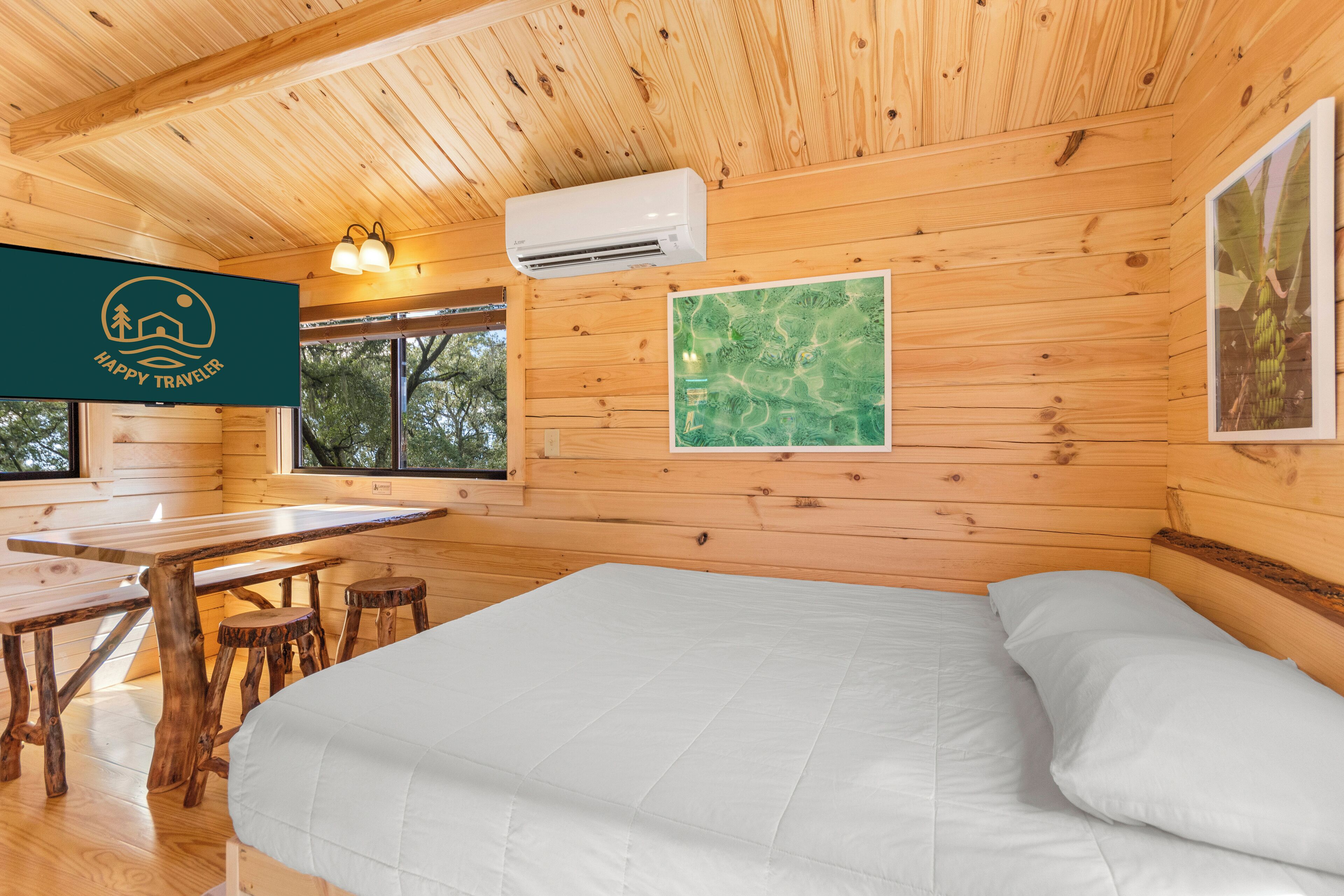 A wooden cabin with a bed, a table, and two stools.