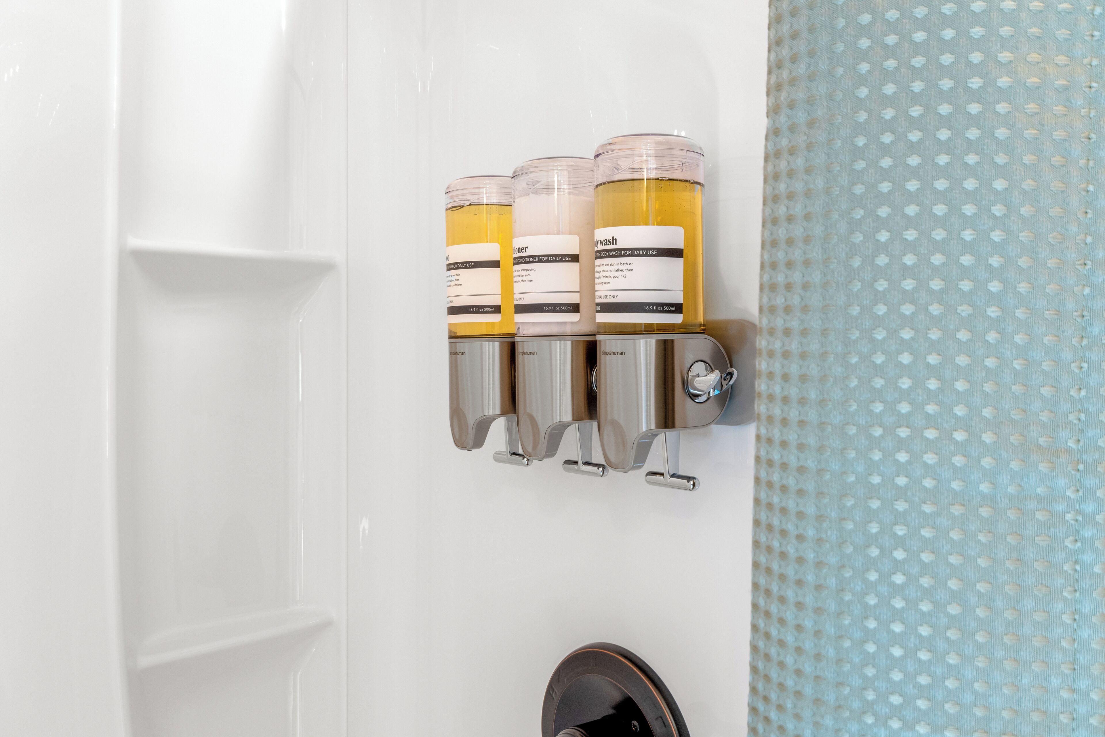 A bathroom with a wall-mounted soap dispenser and a shower curtain.
