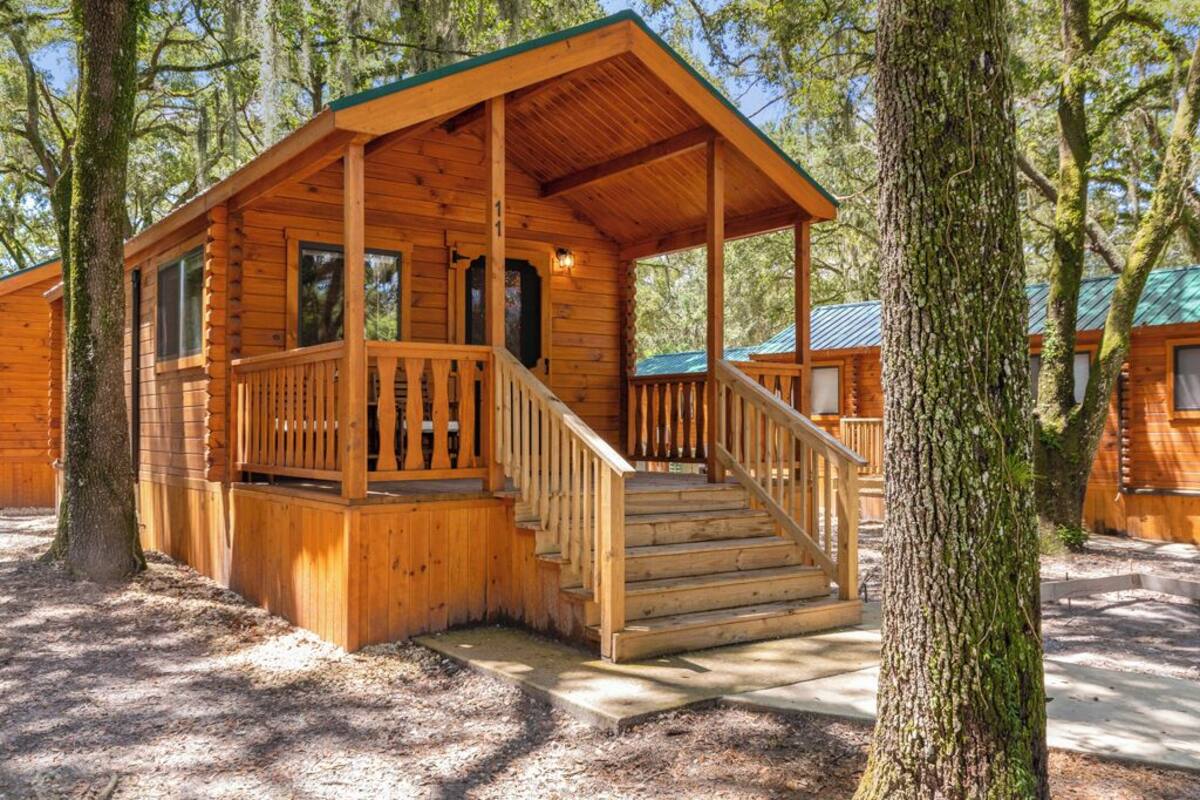 A wooden cabin with a porch and stairs, surrounded by trees.