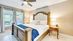 Un dormitorio con una cama grande, un ventilador de techo, una mesita de noche con lámpara y una ventana con cortinas.