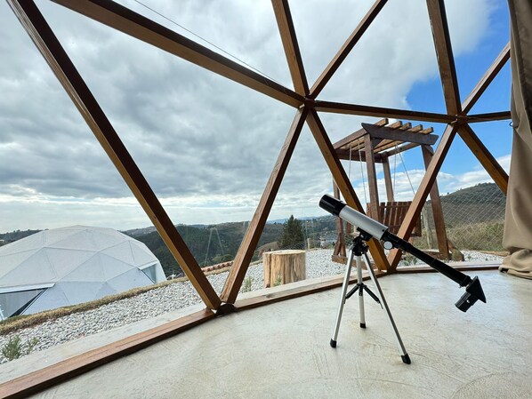 A telescope on a tripod inside a geodesic dome structure with a view of a mountainous landscape. - Domo Geodésico com banheira (Campos do Jordão)