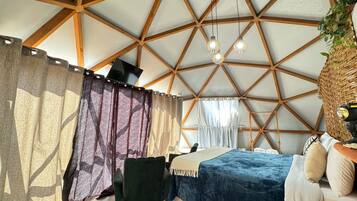 A room with a geometric wooden ceiling, a bed with a blue and white duvet, a green chair, and a woven plant basket.