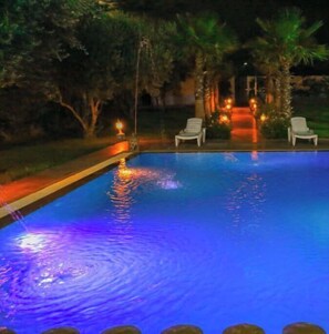 Relax by the pool surrounded by lush greenery and palm trees.