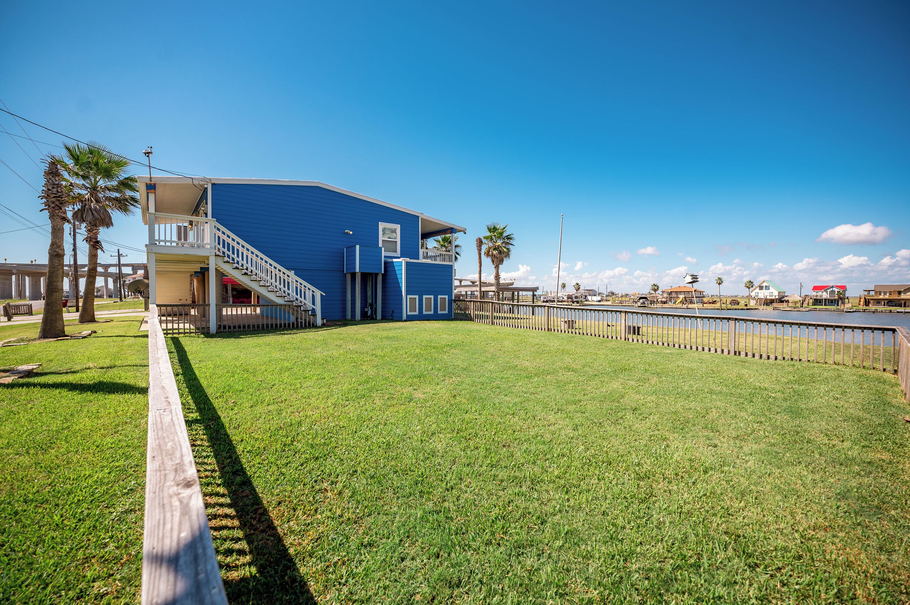 A blue building with a balcony, surrounded by a grassy area and a fence.