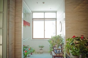 A narrow hallway with a large window, potted plants, and a wooden floor. - Nantong White-collar INN (Nantong)