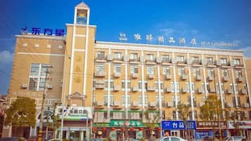 Un hotel de varios pisos con una imponente torre de reloj, varios balcones y una variedad de locales comerciales en la planta baja.
