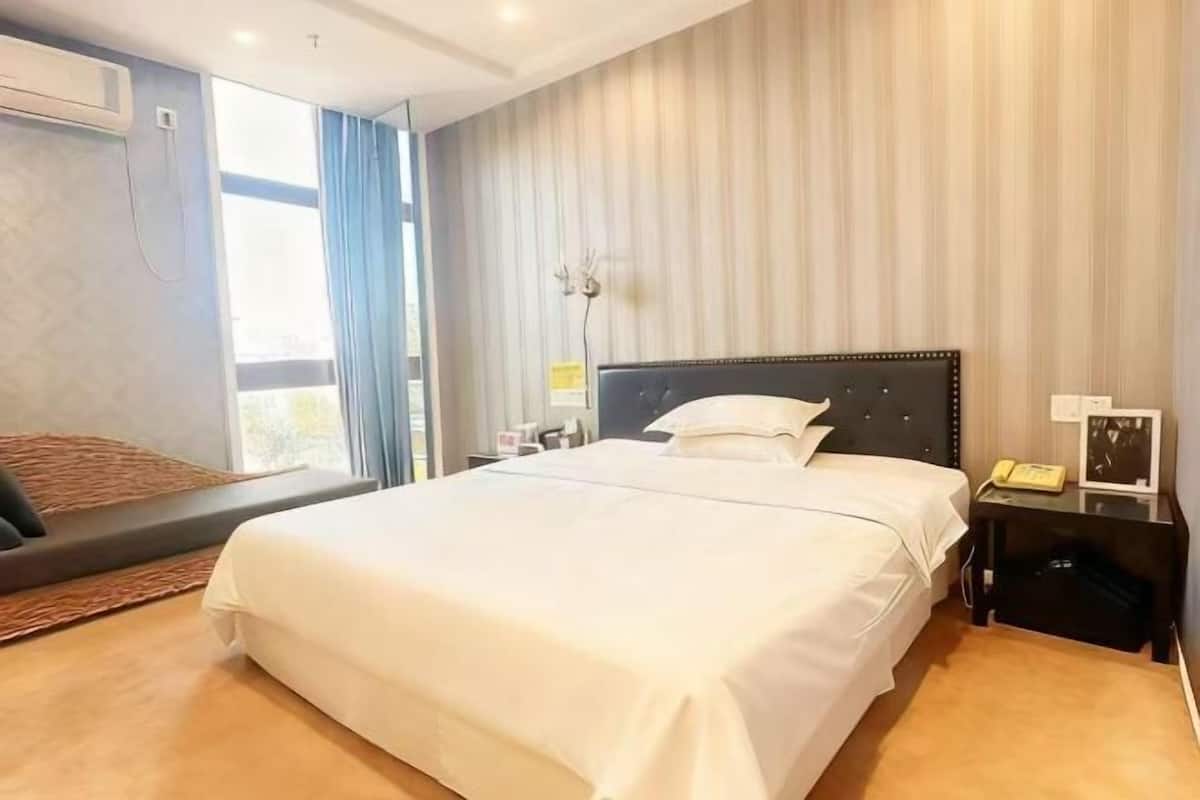 Une chambre d’hôtel avec un grand lit, une table de chevet avec une lampe et une fenêtre avec des rideaux.