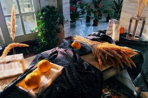 Ein Zimmer mit einem großen Fenster, einer Topfpflanze, einem Holztisch mit einer Zitronenschale und einer Vase mit einer Kerze.