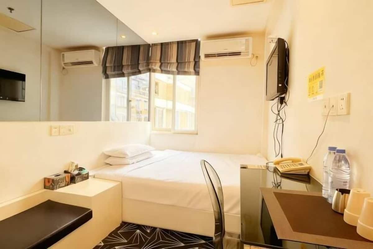 Une chambre d’hôtel avec un lit, un bureau, une chaise, une télévision et une fenêtre avec des rideaux.