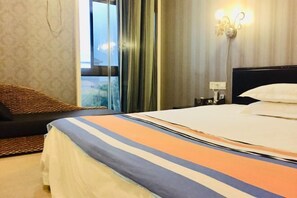 Quarto de hotel com cama, mesa de cabeceira, luminária e vista pela janela com cortinas.