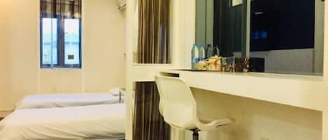 Une chambre d’hôtel avec un lit, un bureau et une chaise, une fenêtre avec des rideaux et une petite table sur laquelle sont posées des bouteilles.