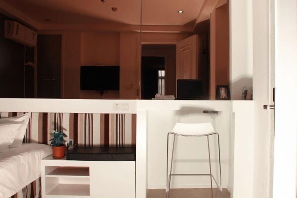 Quarto de hotel moderno com uma cama, uma televisão, uma mesinha e uma cadeira.