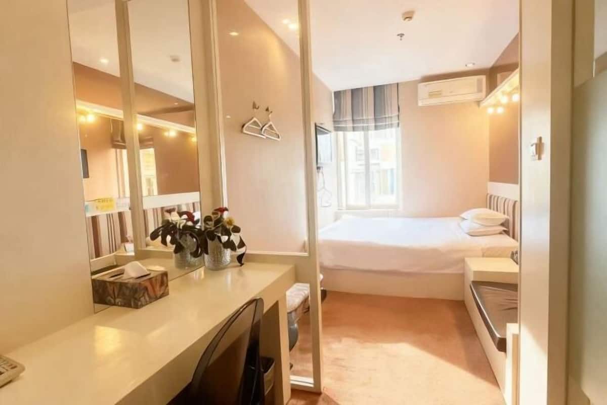 Une chambre d’hôtel de taille réduite, comprenant un lit, une table de chevet et un grand miroir.