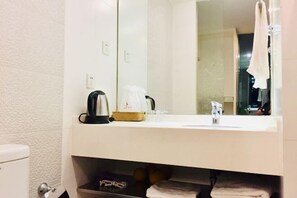 Casa de banho com lavatório, espelho, toalheiro e prateleira com produtos de higiene pessoal.