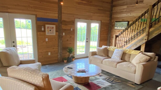A spacious living room with a beige sofa, two armchairs, a coffee table, and a staircase leading to an upper level.