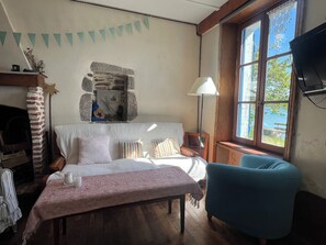 Una habitación acogedora con cama, mesa, silla, pared de piedra, ventana con vistas y televisor.