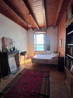 Un dormitorio con cama, escritorio, estantería, ventana con vistas y techo de madera.