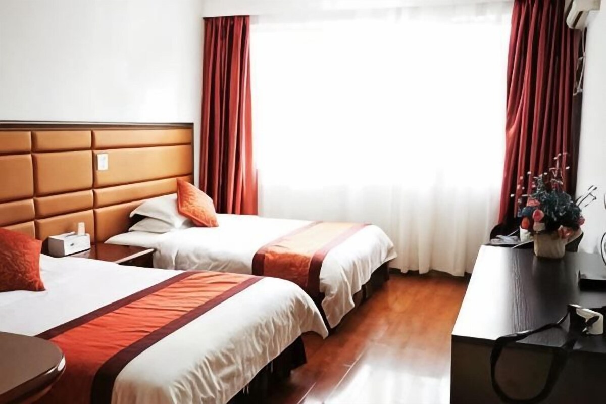 A hotel room with two beds, a wooden headboard, a desk, and a window with curtains.