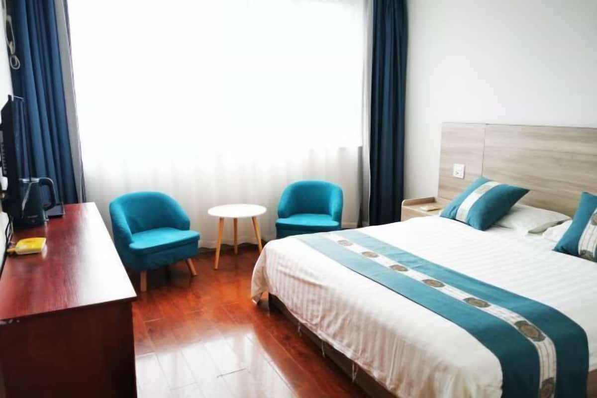 A hotel room with a bed, two chairs, a small table, a desk, and a window with curtains.