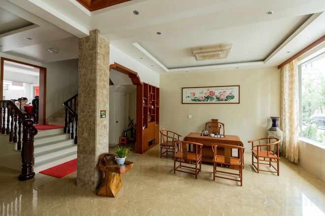 A spacious living area with a wooden dining table, chairs, a red carpet, a staircase, and a large window.