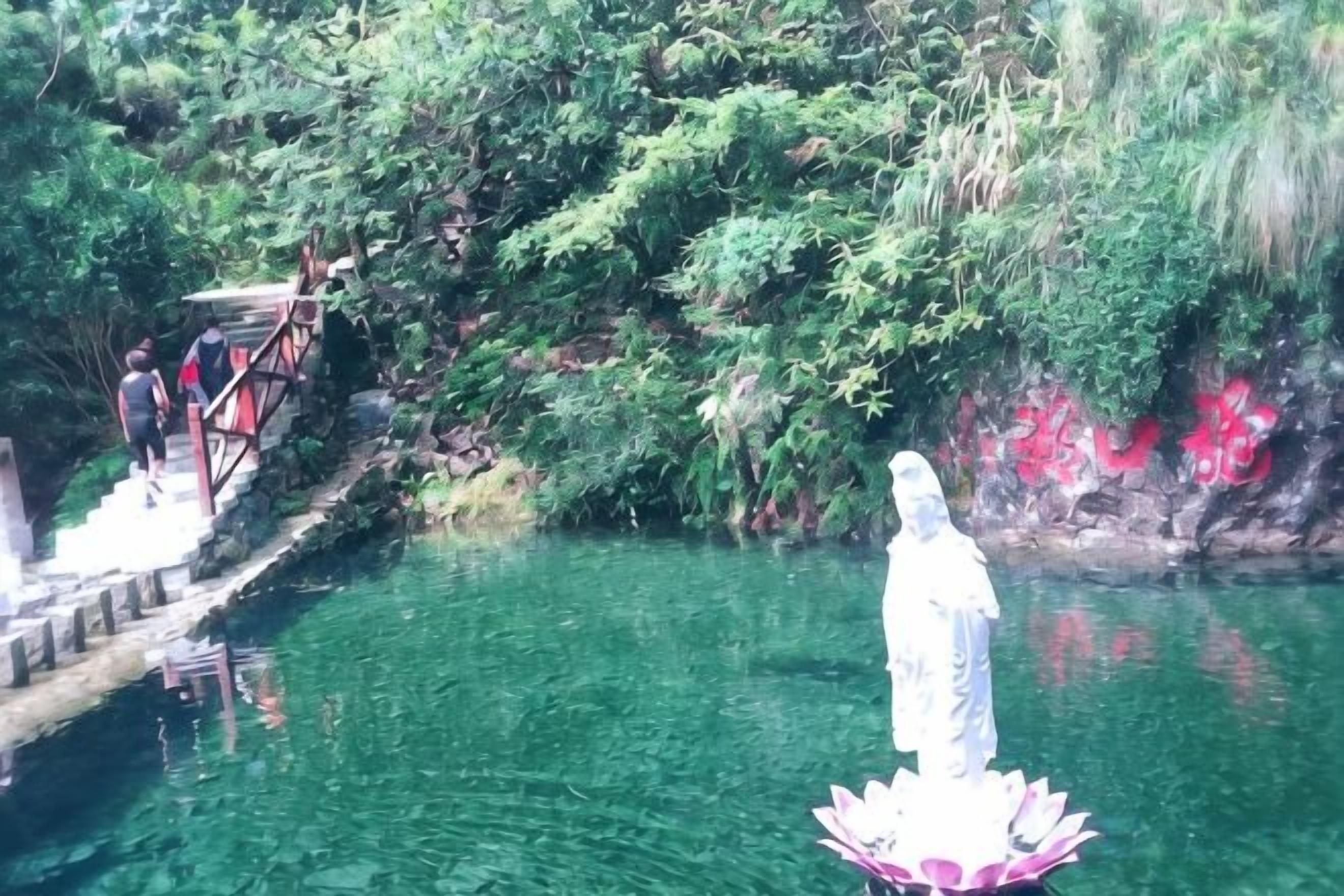 A statue on a lotus base by a clear water body with a staircase and greenery in the background.