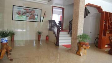 A lobby with a staircase, potted plants, and a framed artwork on the wall.