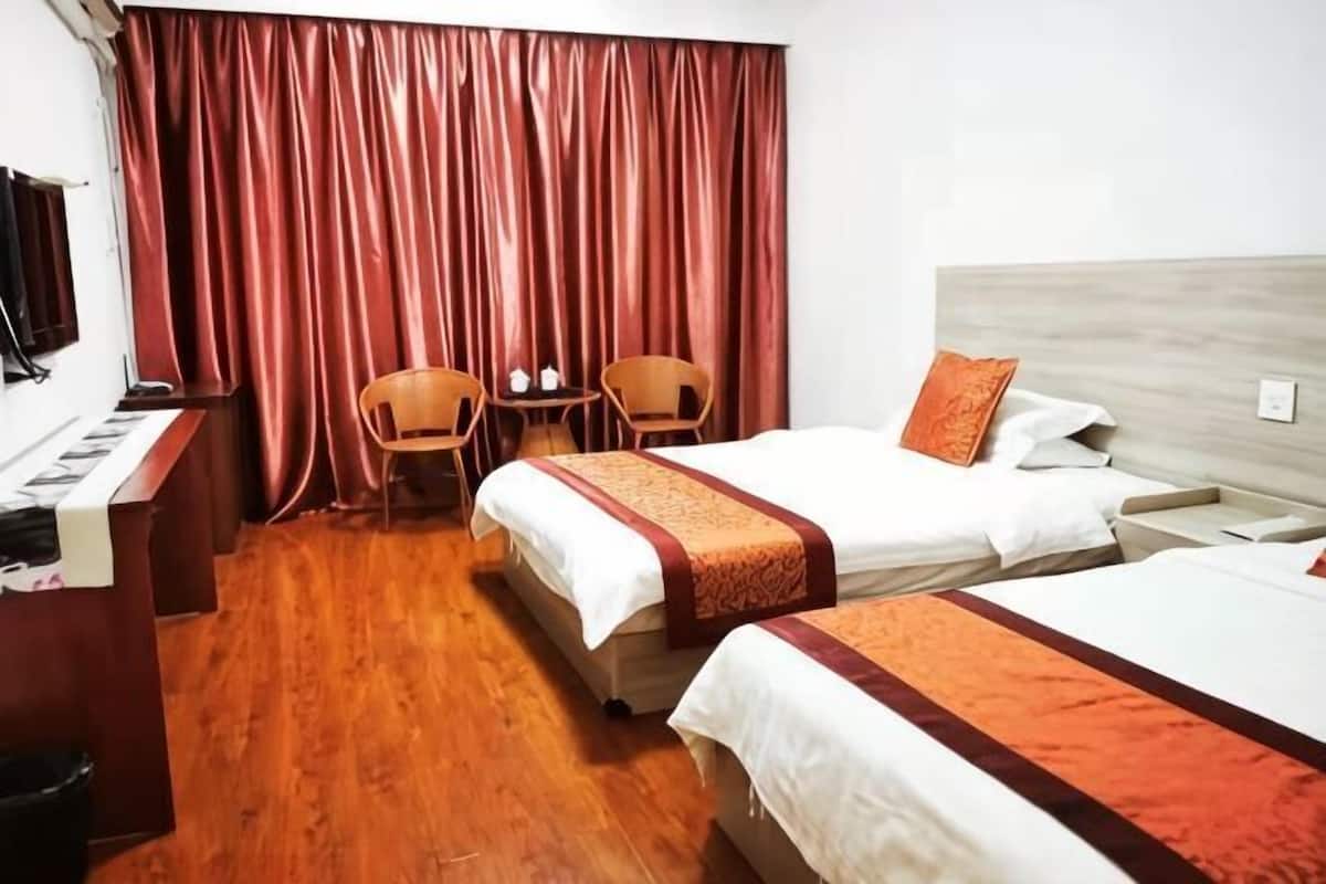A hotel room with two beds, a desk, a chair, and a small table.