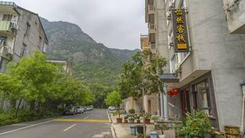 A street view with a building featuring a sign in a foreign language, a mountain in the background, and parked cars along the road.