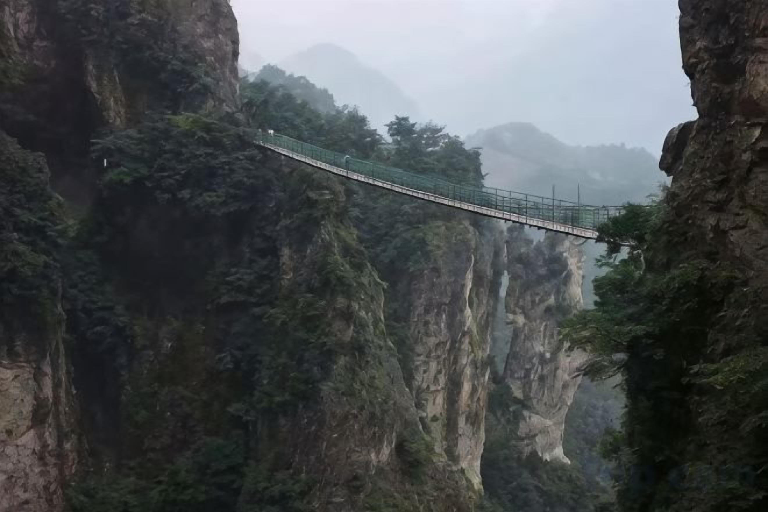 A suspension bridge in a mountainous area with steep cliffs and dense vegetation.