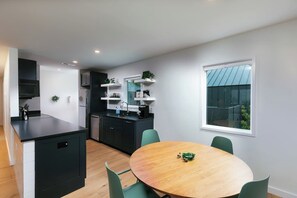 A modern kitchen with black cabinets, a wooden dining table, and a window with a view. - Longleaf Cottage-Walk to Azalea Park (Summerville)