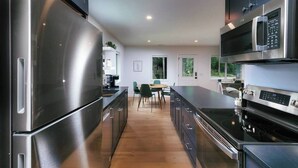 Una cocina moderna con electrodomésticos de acero inoxidable, un comedor con sillas y vistas a través de las ventanas.