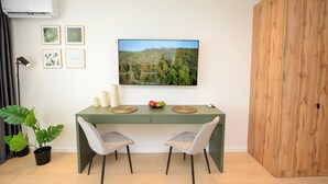 Un coin repas moderne avec une table verte, deux chaises, un grand tableau encadré représentant une forêt et une plante en pot.