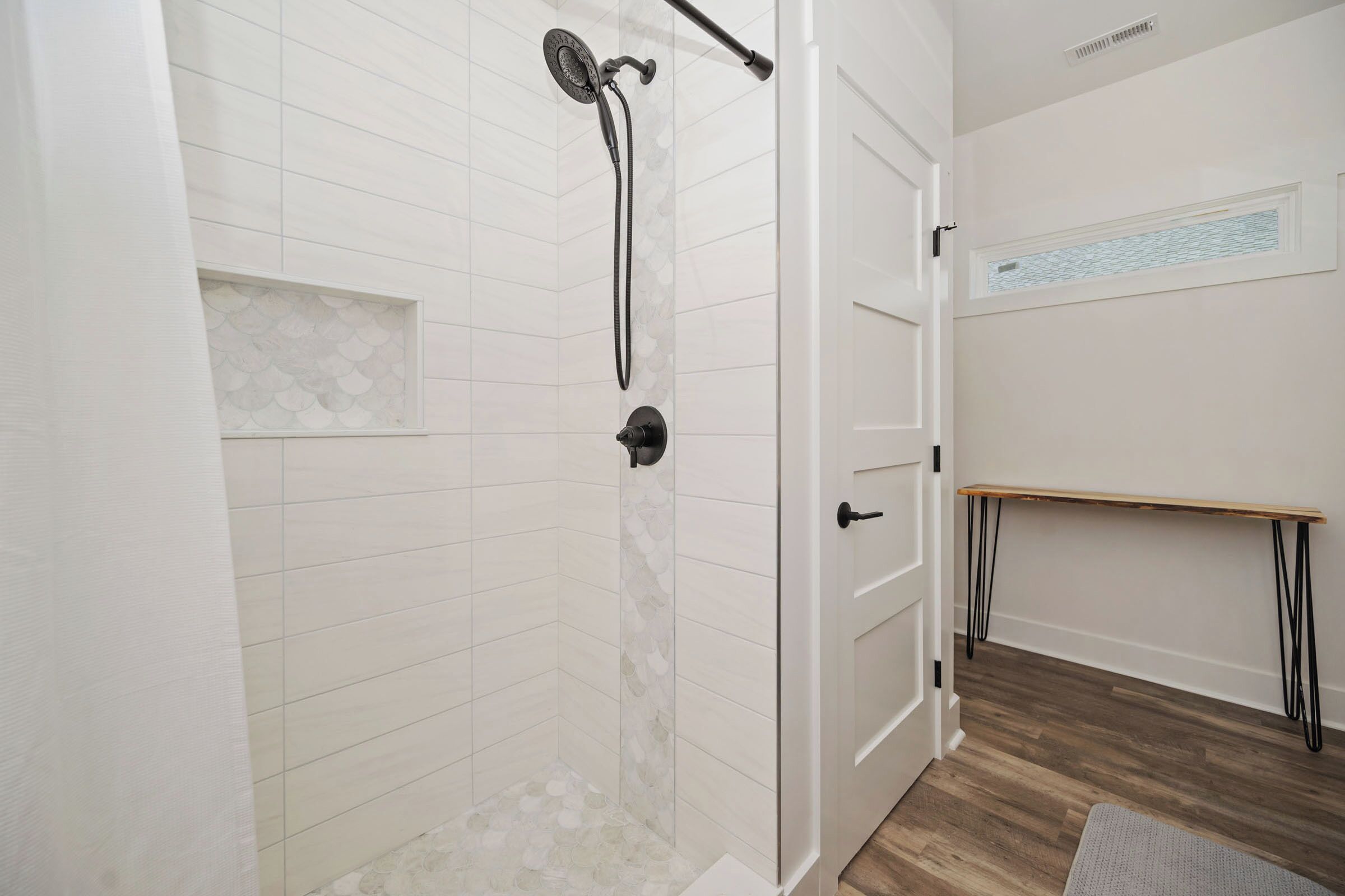 Een badkamer met een douche, een wastafel met spiegel en een houten bankje.