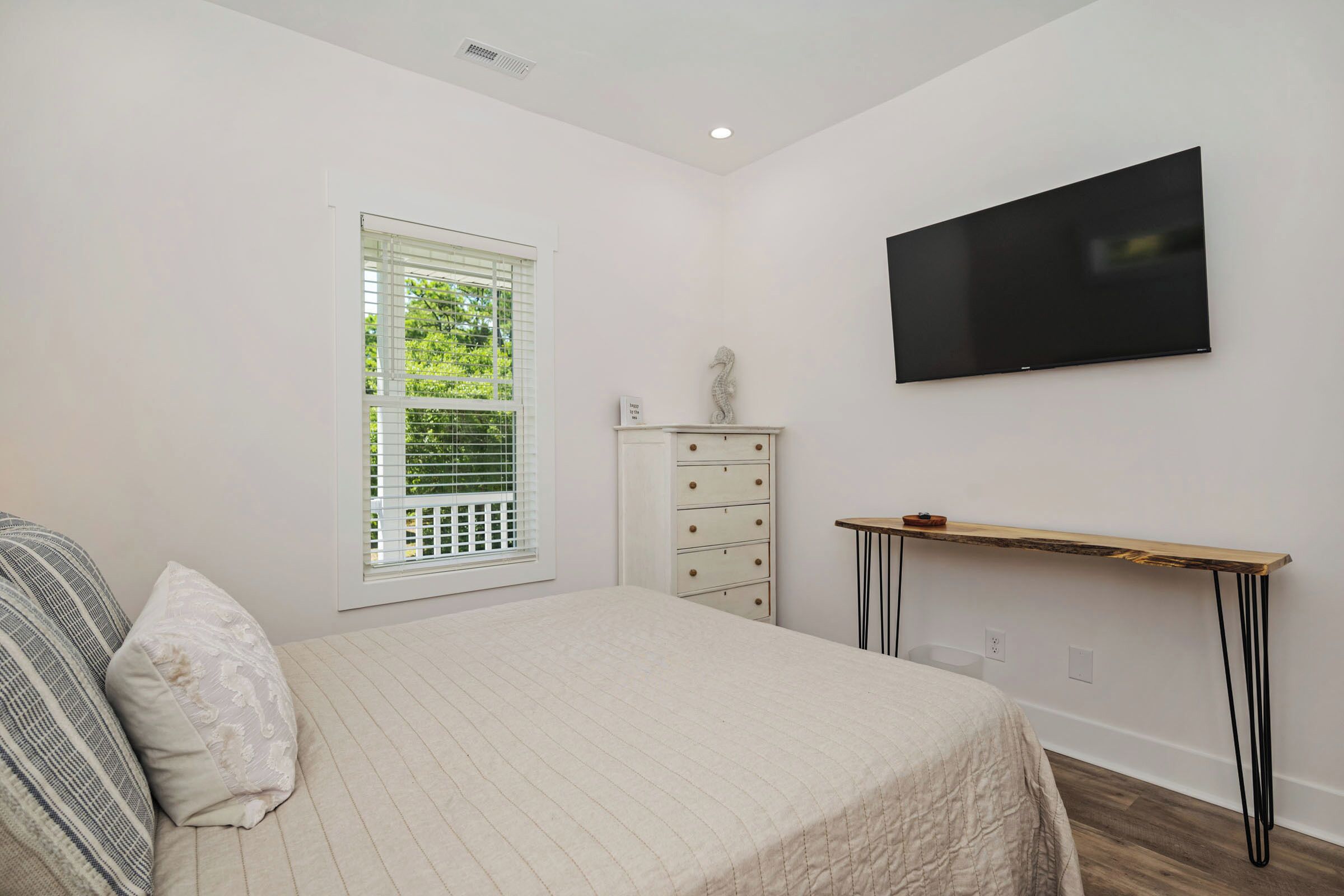 A bedroom with a bed, a dresser, a television, and a window with blinds.