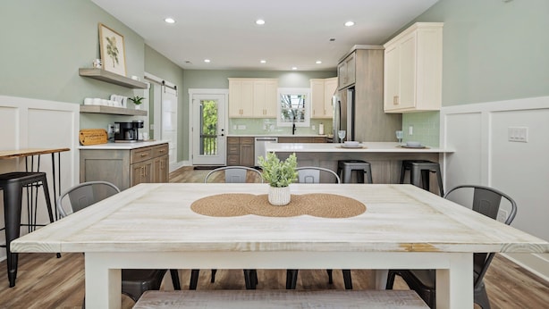 A modern kitchen with white cabinets, a dining table with a placemat, and a small potted plant. - Heads Carolina: Modern Home with Private Pool in Quiet Neighborhood (Oak Island)