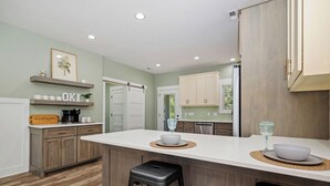 A modern kitchen with wooden cabinets, a white countertop, and a bar stool. - Heads Carolina: Modern Home with Private Pool in Quiet Neighborhood (Oak Island)