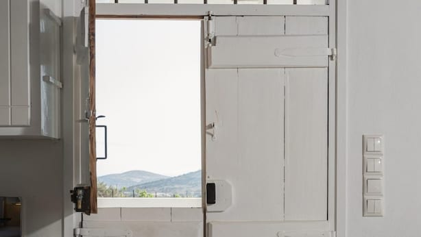 A white door with a window, a light switch, and a small vase with flowers. - Kottakis Stone House (Naxos)