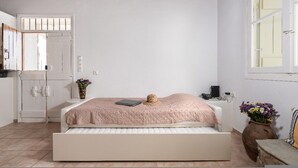 A bedroom with a bed, a window, a door, and a vase with flowers. - Kottakis Stone House (Naxos)