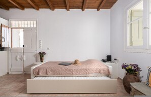 A bedroom with a bed, a window, a door, and a vase with flowers.
