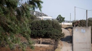A rural road leading to a white house with a fenced yard and a hill in the background. - Kottakis Stone House (Naxos)