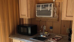 A compact kitchen with wooden cabinets, a microwave, a sink, and a refrigerator.