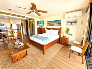 A hotel room with a bed, a desk, a chair, a ceiling fan, and a view of the beach.