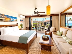 Une chambre d’hôtel comprenant un lit, un canapé, une table basse, un ventilateur de plafond et une vue sur la piscine et les bâtiments environnants.