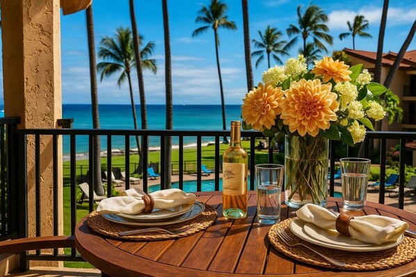 A wooden table set for two with plates, napkins, a bottle of wine, and a vase of flowers, overlooking a beach with palm trees and a clear sky.