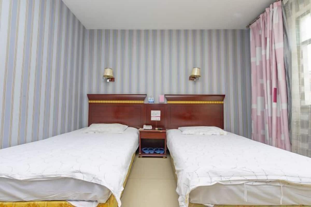 A hotel room with two single beds, a wooden headboard, a nightstand with a lamp, and striped wallpaper.