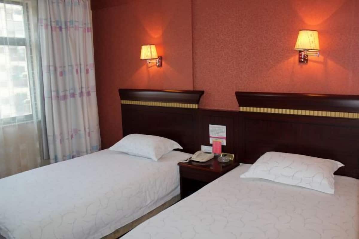 A hotel room with two single beds, a nightstand with a phone and a lamp, and a window with curtains.