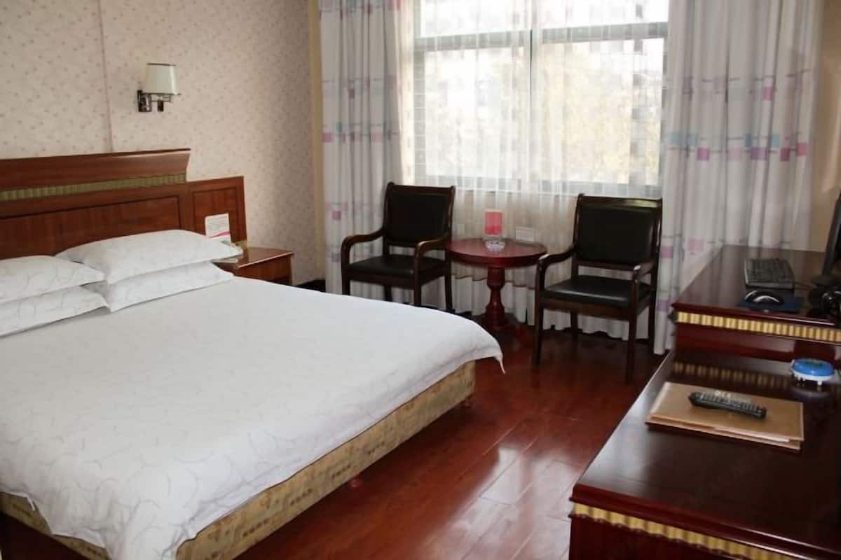 A hotel room with a bed, two chairs, a small table, a desk with a keyboard, and a lamp.