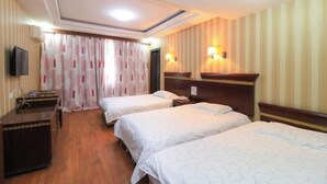 A hotel room with three single beds, a wooden dresser, a flat-screen TV, and two wall-mounted lamps.