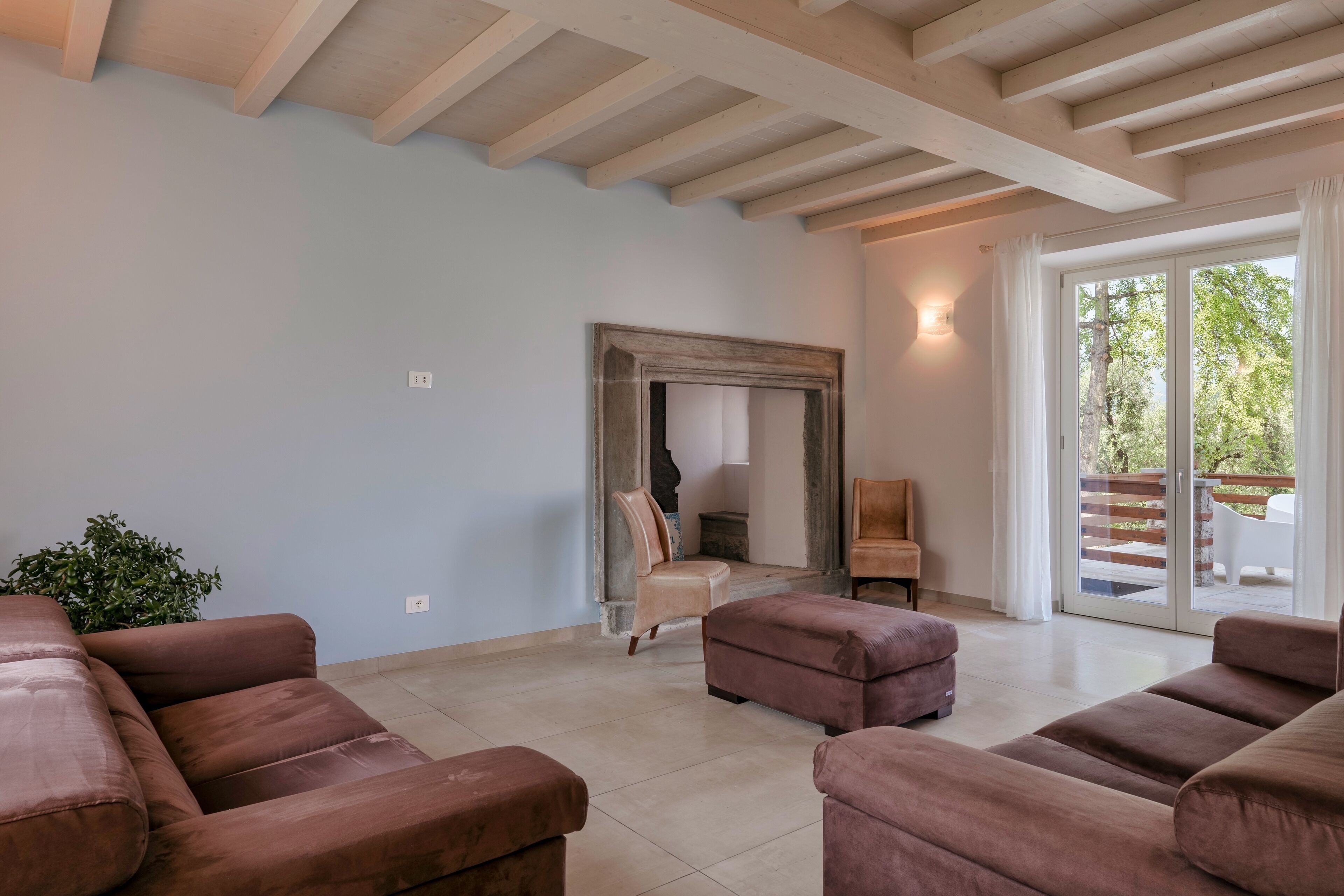Un soggiorno spazioso con una grande finestra, un soffitto in legno e un'ampia porta scorrevole in vetro che dà su un'area esterna.